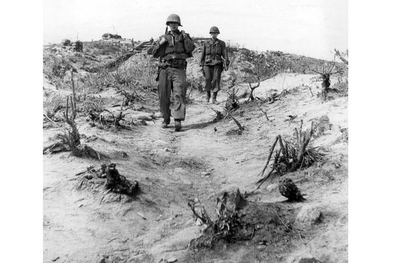 Two U.S. Army soldiers walking across barren, shell-scarred Korean hill terrain after battle, 1952-1953