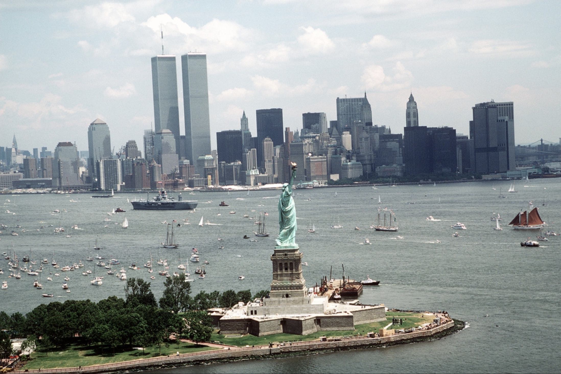 The Twin Towers of the World Trade Center rising above the Lower Manhattan skyline, seen from New York Harbor beside the Statue of Liberty