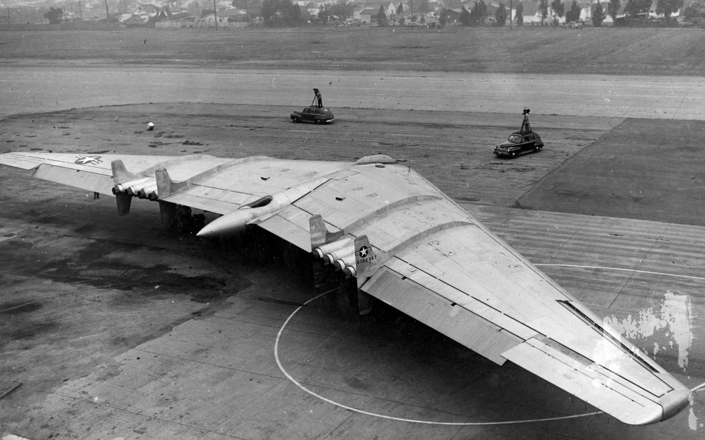 Northrop YB-49 Flying Wing taking off, exhaust smoke trailing, spectators watching — Muroc Army Air Field, California